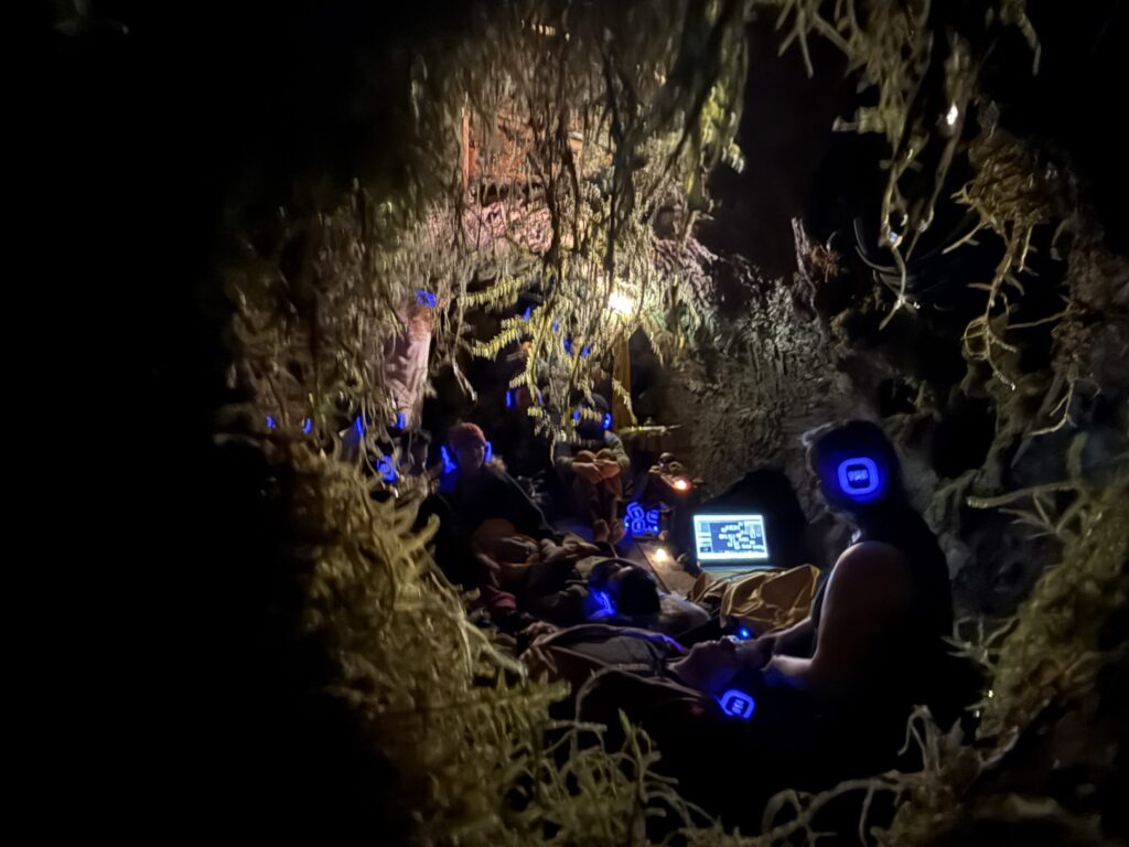 A woman caressing a person laying down on cushions inside a mossy temple at night